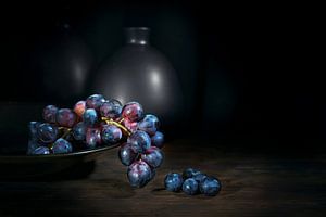 Paarsblauwe druiven in een schaal op een rustieke houten tafel met vazen