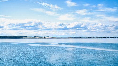 Een rustig zeegezicht onder een heldere hemel. Het water weerspiegelt zachte wolken.