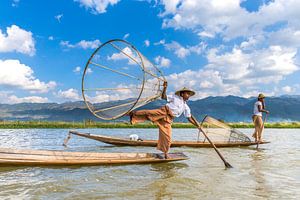 Visser die met traditionele boot op het Inle meer in Myanmar op ouderwetse wijze met een vis korf vi