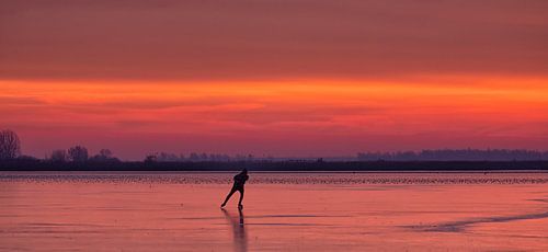 Een schaatser op het ijs van het Lauwersmeer tijdens zonsopkomst in de winter