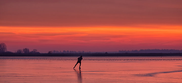 Een schaatser op het ijs van het Lauwersmeer tijdens zonsopkomst in de winter van <span class="secondary-font">Bas Meelker</span>