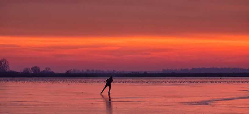 Een schaatser op het ijs van het Lauwersmeer tijdens zonsopkomst in de winter van Bas Meelker