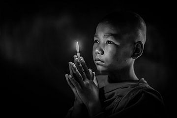 BAGHAN, MYANMAR, 10 DECEMBER 2015 - YOUNG MONK with lighted candles in hand meditating IN MONASTERY  by Wout Kok
