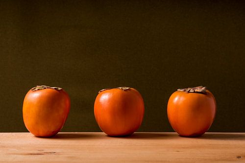 drie sharonfruit op een rij.