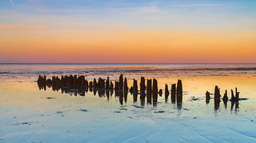 Poteaux en bois (brise-lames) dans la mer des Wadden à Wieringen au coucher du soleil sur Bram Lubbers
