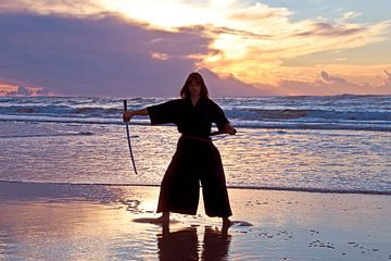 Jonge samurai vrouw met Japans zwaard(Katana) bij zonsondergang op het strand van Eye on You