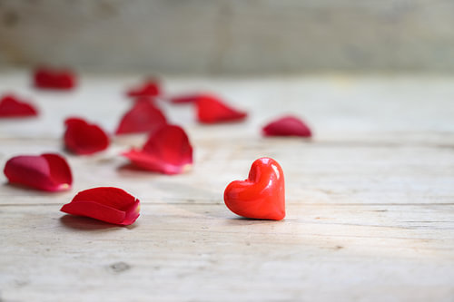 rotes Herz aus Glas und Rosenblättern auf rustikalem grauem Holzgrund, Liebeskonzept mit Kopierraum,
