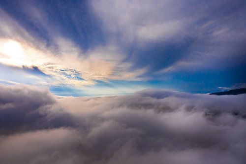 Blue and dark clouds swirl below, dark blue sky, aerial photo.