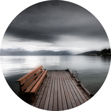 Een mystiek landschap in Noorwegen in zwart-wit met een meer. Een leeg bankje staat op een steiger b van Bas Meelker