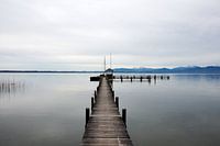 Serene image of a wooden jetty in Lake Chiemsee with a winter mountain landscape in the background.