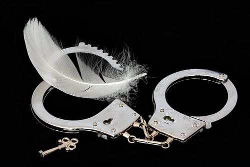 Handboeien, sleutel en witte veer