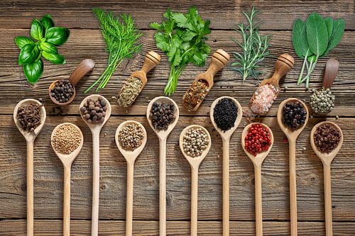 Kleurrijke verscheidenheid aan specerijen in lepels op een houten plank