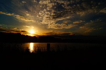 Zonsondergang met reflectie in het water en bewolkte lucht