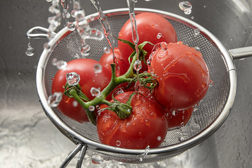 frische Tomaten in einem Metalltopf unter vielen Wassertropfen, waschen und gesundes Essen zubereite