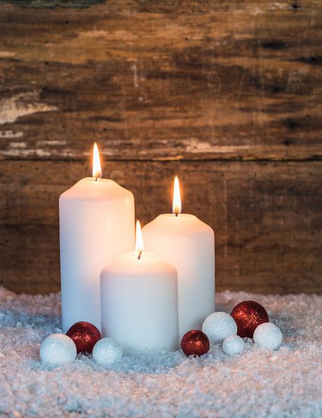 Three Christmas candles with red and white ornaments on snow by Alex Winter