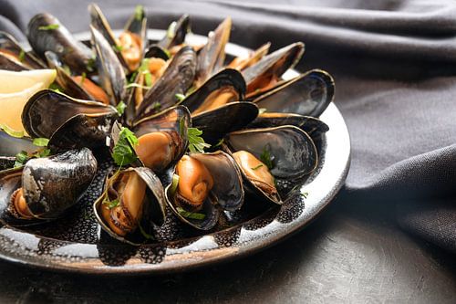 Freshly cooked blue mussels with lemon and parsley garnish on a plate, dark napkin and slate table, 