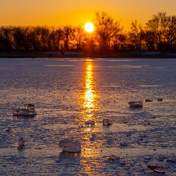 Chunk of ice on a frozen lake during a warm sunrise by Kim Willems