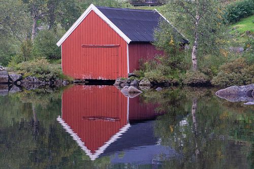 Mirrored wooden boathouse on the lake in Norway