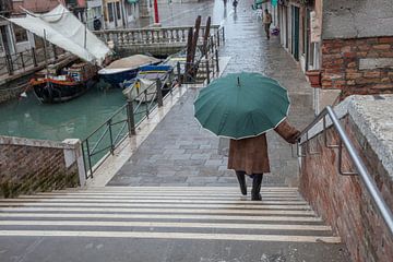 Dame met paraplu langs kanaal in centrum Venetie, Italie met veel regen van Joost Adriaanse