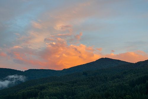 Ciel orange dramatique au coucher du soleil sur des montagnes couvertes de forêts