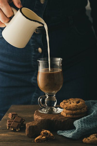 Frau gießt Milch in Glas mit Kaffee ein von Iryna Melnyk