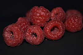 Red raspberries on black background. by Heidi Pype