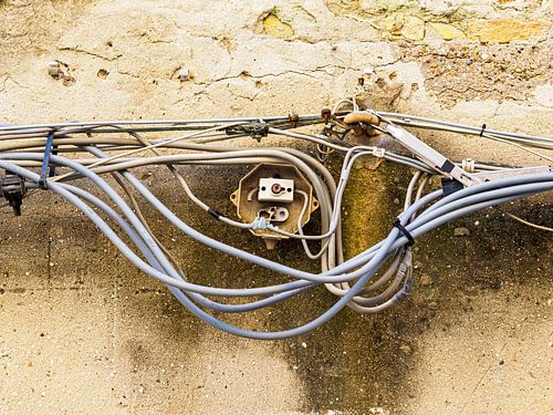 Verwarde draden en kabels die aan een oude betonnen muur vastzitten