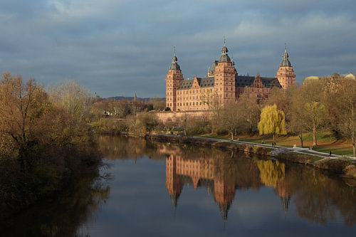 Schloss Johannisburg am Ufer des Mains mit Spiegelung im dunkelblauen Wasser, berühmtes historisches
