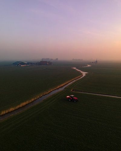 Tracteur rouge dans un paysage de polders brumeux au lever du soleil