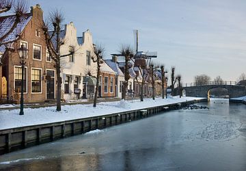 Winterse aanblik van een rij historische huizen en molen in Sloten van Henk Vrieselaar