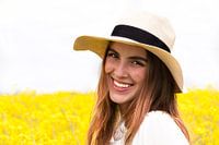 Portrait of a young woman with a straw hat in front of a yellow flower field