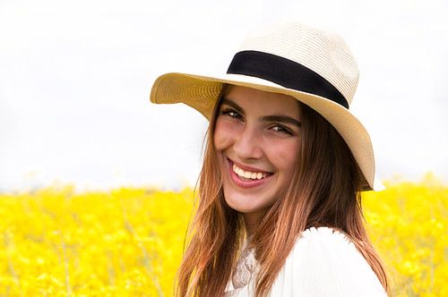 Portret van een jonge vrouw met een strohoed voor een geel bloemenveld