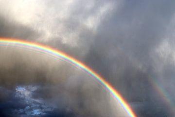 Een dubbele regenboog boven een meer voor een onweersbui