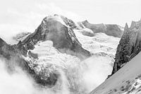 Rugged glaciated mountain top protrudes above the clouds in black and white