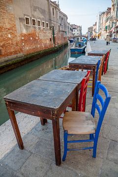 Tafeltjes met stoelen aan kanaal met boten in oude centrum Venetie, Italie