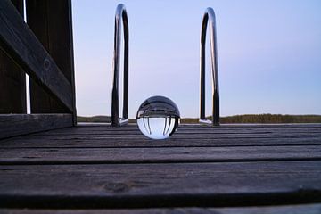 Glazen bol op een loopbrug die in een meer reikt van Martin Köbsch