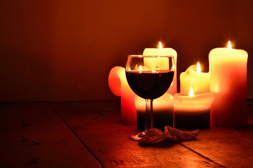 Wijnglas gevuld met rode wijn en kaarslicht in het donker. van Mariëtte Plat