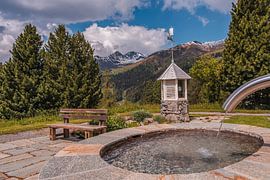 Holzbank bei einem Brunnen inmitten der Berge von Dafne Vos