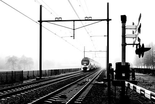 Zwart-wit foto van een Hollandse trein in mist bij spoorwegovergang