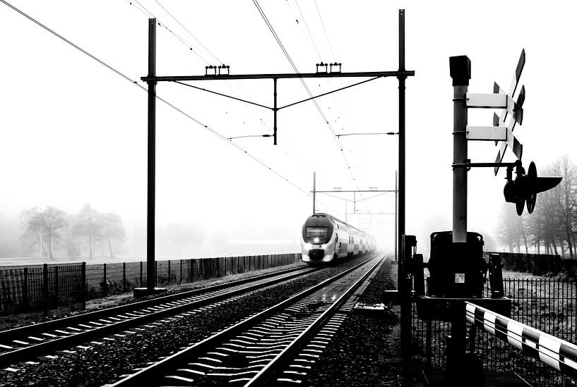Zwart-wit foto van een Hollandse trein in mist bij spoorwegovergang by Hans Post