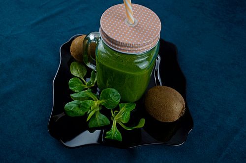 Bladsalade en kiwi smoothie op zwart bord versierd met kiwi en veldsla