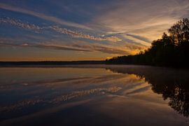 Dawn over the quiet water surface of the lake. The morning blue sky is lit by the orange light of th by Michael Semenov