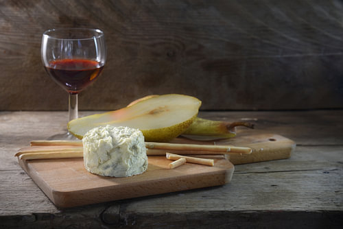 cremig-blauer Stiltonkäse, Portwein, Birne und einige Knabberstangen auf einem Schneidebrett vor ein