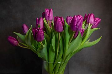 ein Strauß lila Tulpen in einer Vase mit dunklem Hintergrund