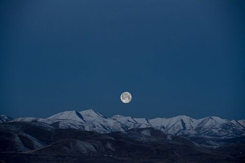 Volle maan boven besneeuwde bergtoppen
