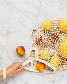 Eine Hand, die eine Baumwoll-Netz-Tüte mit frischen Zitronen und einem Apfel hält von Lucyna Smulders Photography