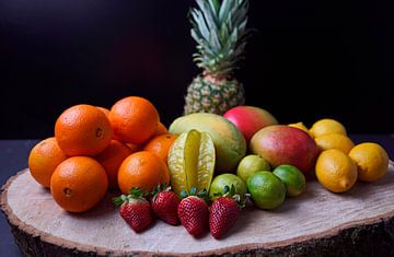 Orangen, Mangos, Papaya, Erdbeere, Ananas, Limetten und Zitronen auf Holzscheibe angeordnet