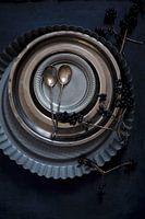 Flan tin, metal plates, pewter plates and silver spoons on black surface