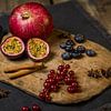 Houten snijplank met granaatappel, passievrucht, bessen, kaneelstokjes en steranijs van Mayra Fotografie