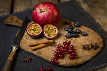 Wooden cutting board with pomegranate, passion fruit, berries, cinnamon sticks and star anise by Mayra Fotografie